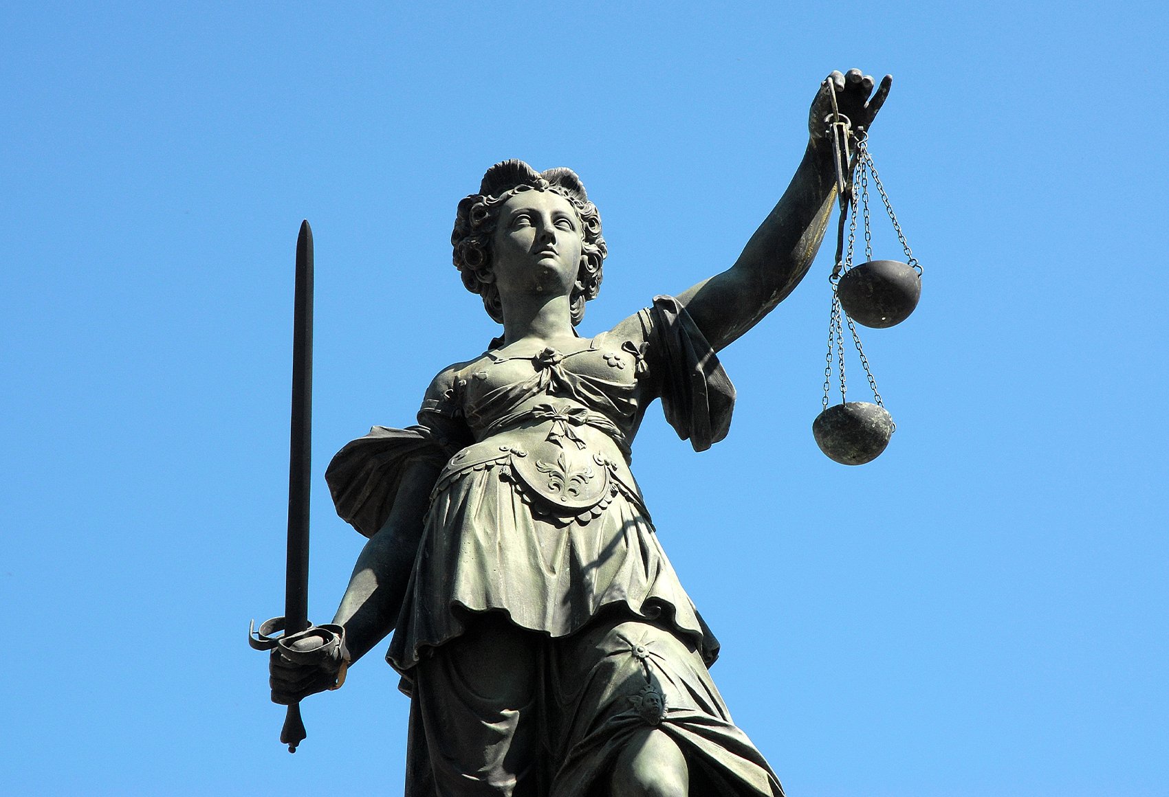 A low-angle, close-up shot of a statue of Lady Justice against a clear blue sky.