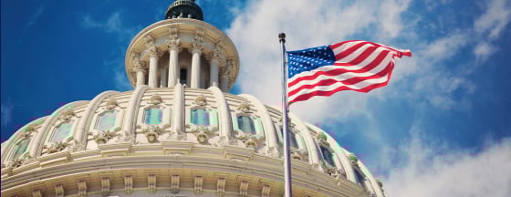 United States Capitol building with flag and sky in foreground and background